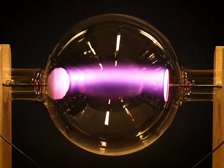 A twelve-inch glass phanotron globe glowing magenta between two wooden supports.